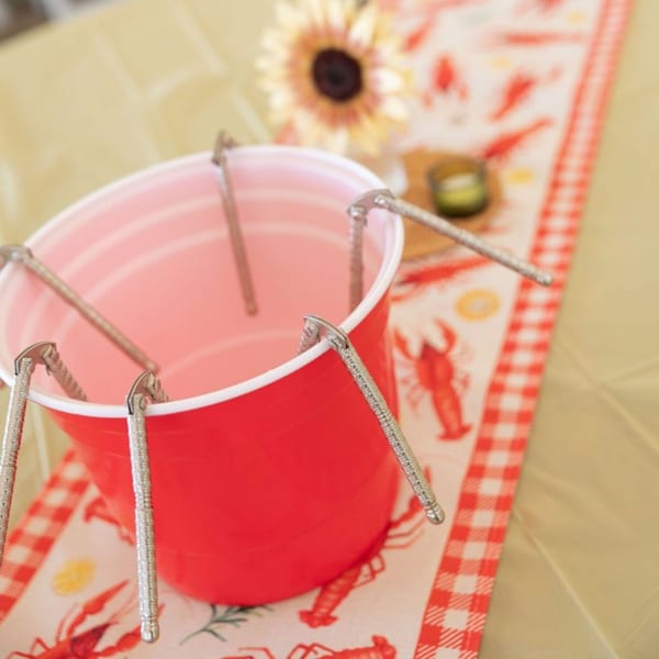 Red plastic cup filled with crab crackers on a crawfish-patterned table runner with a sunflower.