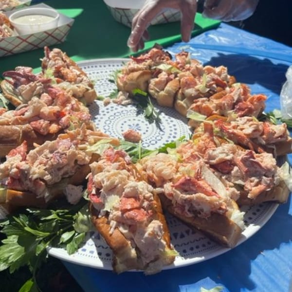 A large platter of lobster rolls, garnished with parsley, on a white patterned plate.