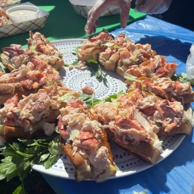 A large platter of lobster rolls, garnished with parsley, on a white patterned plate.