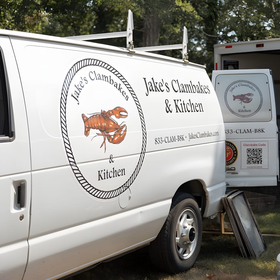 Two white Jake's Clambakes & Kitchen vans with lobster logos parked outdoors.