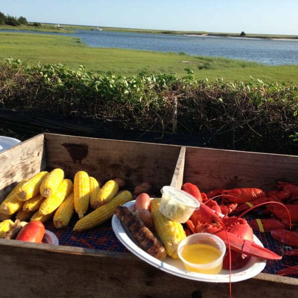 Lobsters, corn on the cob, and potatoes in a wooden crate with a scenic water view.