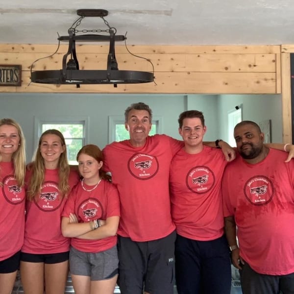 Six smiling people, three women and three men, wearing matching red "Jake's Clambakes & Kitchen" t-shirts.