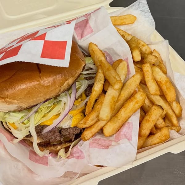 A cheeseburger with lettuce, onions, and cheese, next to a pile of french fries in a takeout container.