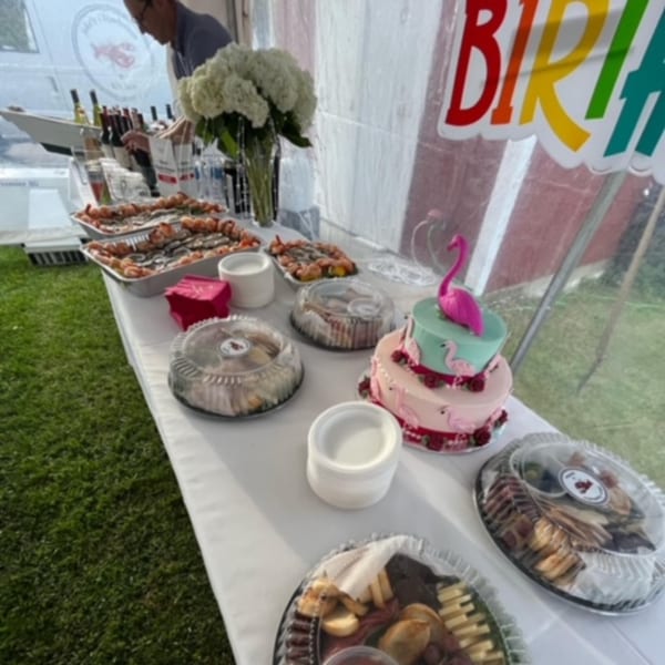 A long table with various appetizers, drinks, and a flamingo-themed birthday cake under a tent.