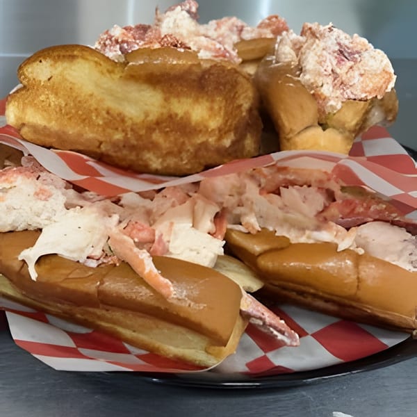 Three lobster rolls, two in red and white checkered paper, overflowing with fresh lobster meat.