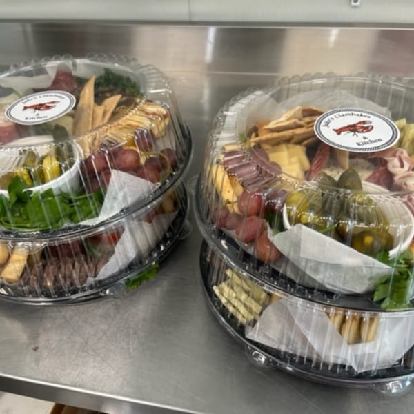 Two stacked charcuterie platters with meats, cheeses, grapes, and crackers, ready for takeout.