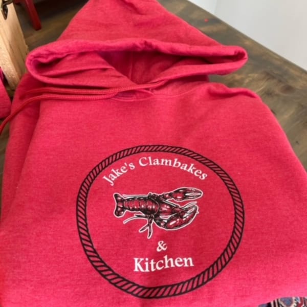 A vibrant red hoodie featuring the "Jake's Clambakes & Kitchen" logo with a lobster graphic.