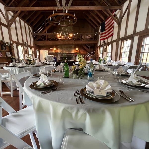 Elegant dining tables set with white tablecloths, place settings, and floral centerpieces in a rustic hall.