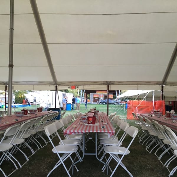 Long tables with red and white checkered tablecloths and white folding chairs under a large tent.