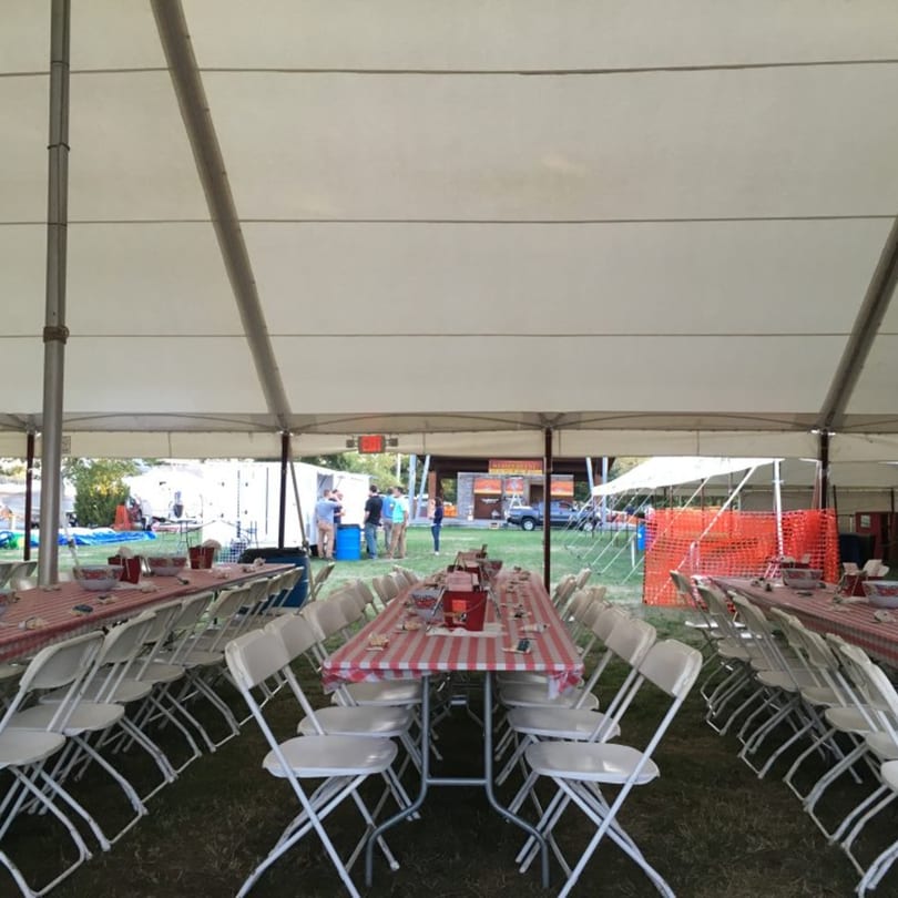 Long tables with red and white checkered tablecloths and white folding chairs under a large tent.