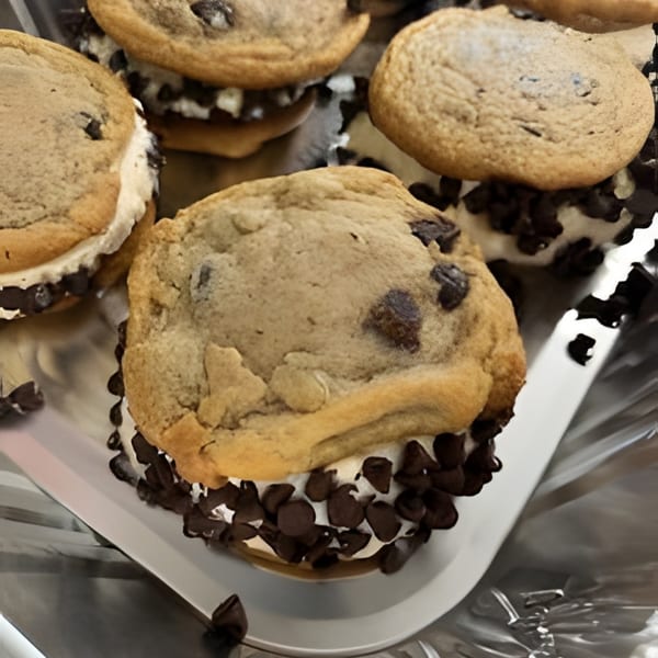Several chocolate chip cookie ice cream sandwiches with mini chocolate chips on a silver tray.