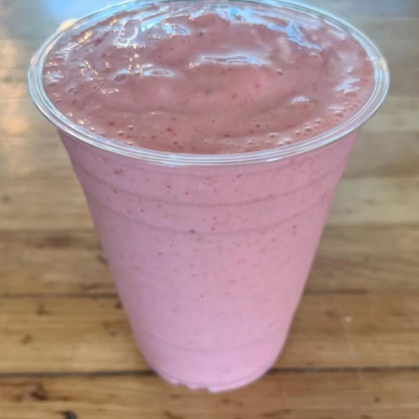 A vibrant pink smoothie in a clear plastic cup, sitting on a rustic wooden surface.