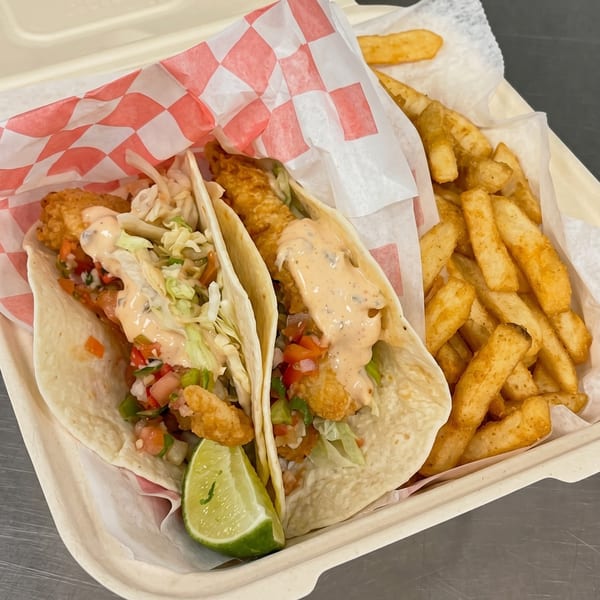 Two fish tacos with sauce, pico de gallo, and a lime wedge, served with french fries.