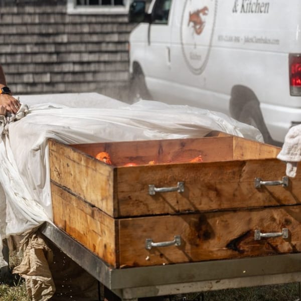 Steaming wooden clam bake boxes with a white catering van in the background.
