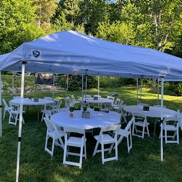 White canopy tent covering round tables with white chairs on a grassy lawn.