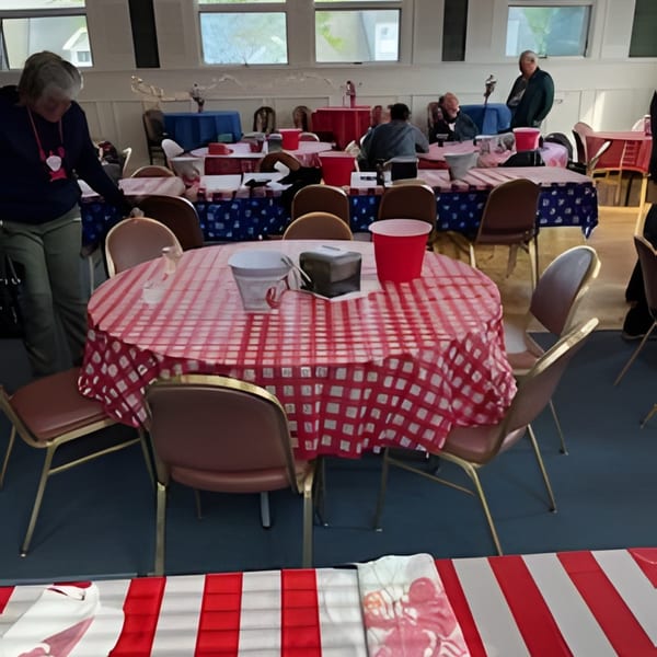 A large room with many tables covered in red and white checkered tablecloths, with people seated.