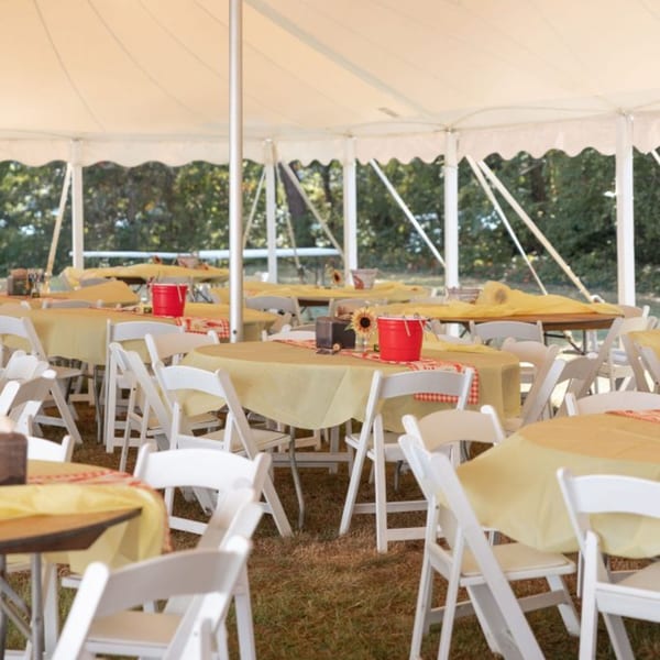 Outdoor event tent with round tables, yellow tablecloths, white chairs, and red buckets.